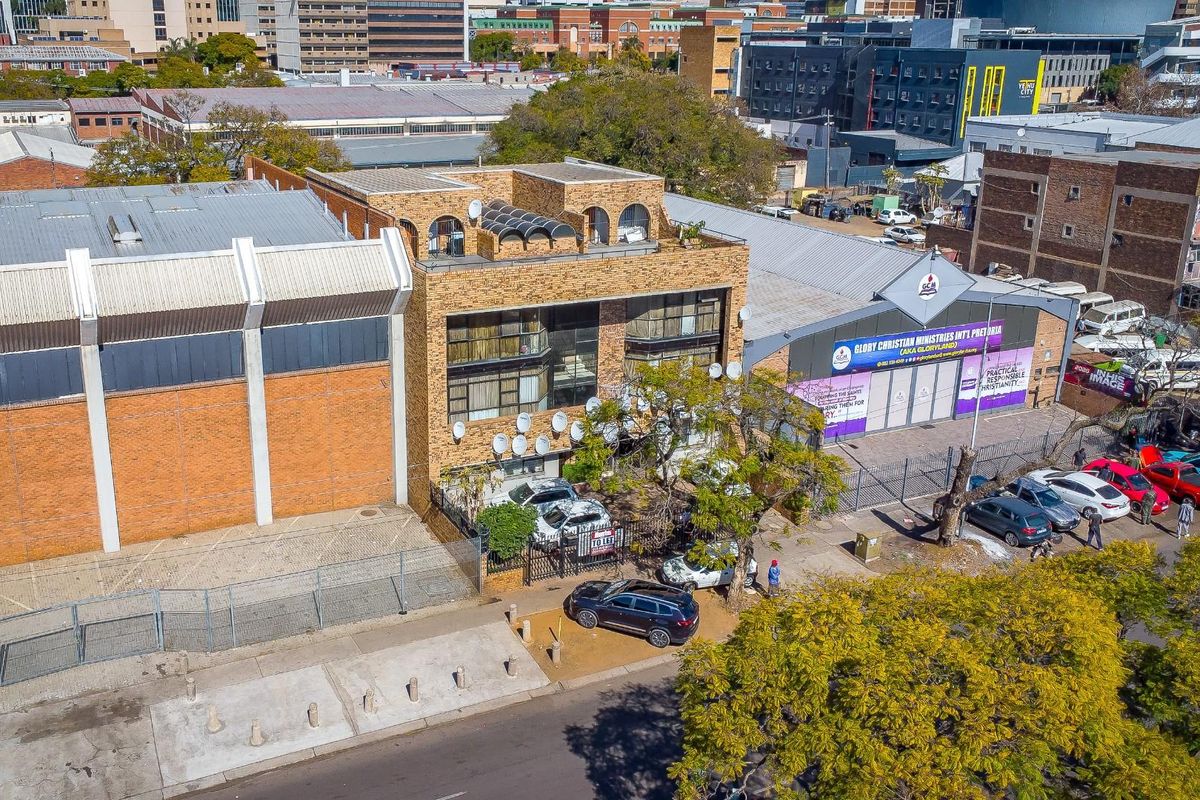 Aerial view of a commercial property featuring a brick building, paved parking area, and security fencing in an urban setting.