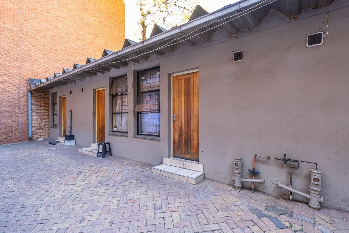 Rear exterior view of a commercial building featuring a paved courtyard, multiple access doors, and exposed exterior plumbing infrastructure.