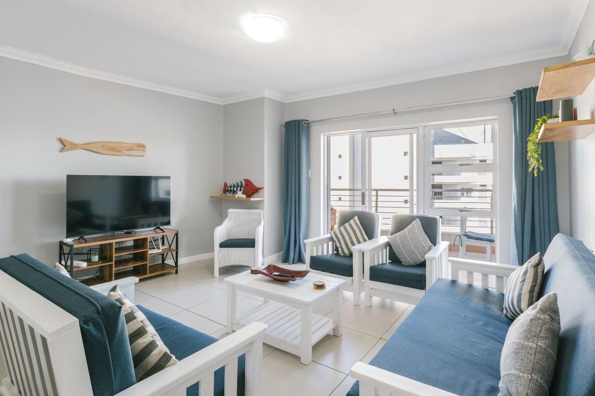 A bright and well-maintained living room featuring neutral tiled flooring, modern ceiling lighting, and a sliding glass door providing access to the balcony.