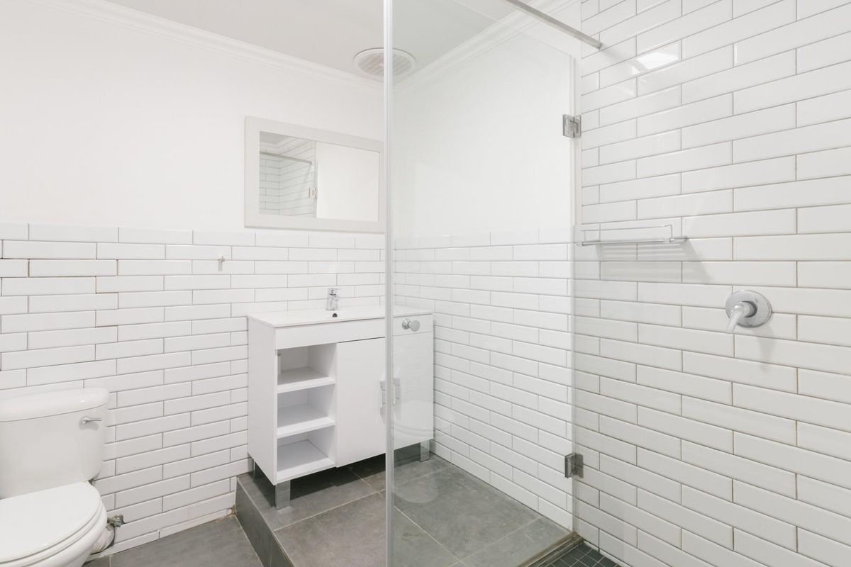 A clean, modern bathroom featuring white subway tile walls, a glass-enclosed shower, and a contemporary vanity unit with grey floor tiles.