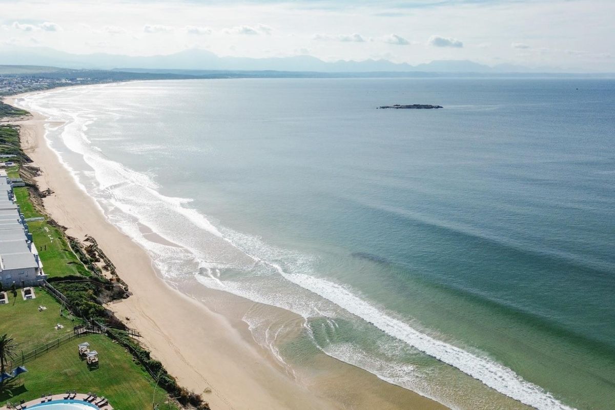 Aerial view of the coastal apartment complex, showcasing direct beach access, landscaped grounds, and a swimming pool overlooking the ocean.
