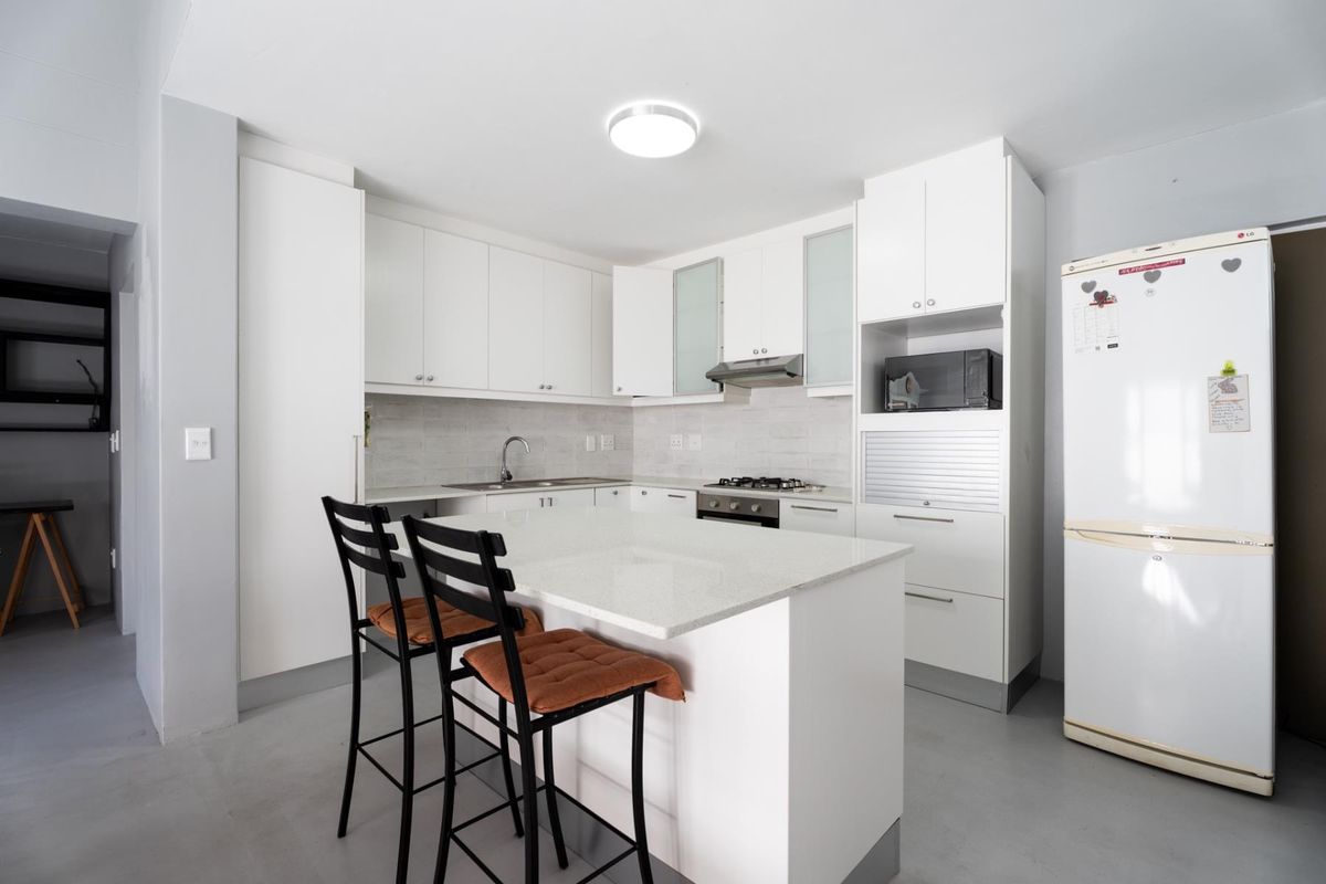 Modern kitchen featuring white cabinetry, stone countertops, a central island with breakfast bar seating, and integrated appliances including a gas hob and extractor fan.
