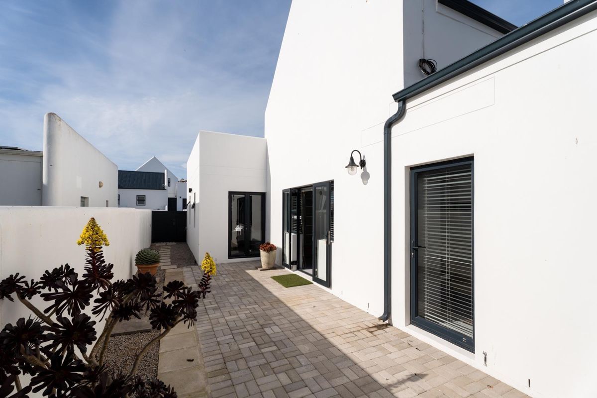 A well-maintained rear exterior featuring a paved patio area, modern white facade, and dark aluminium framed doors leading into the home.