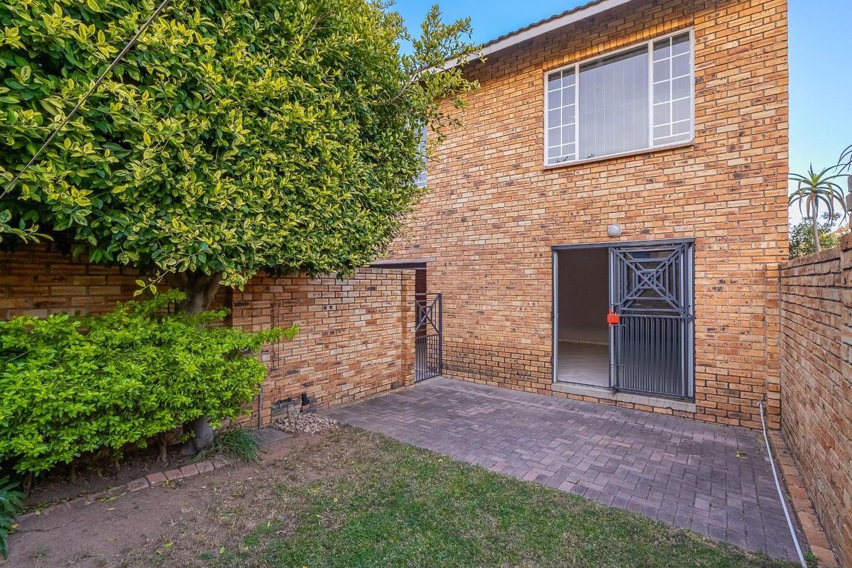 Rear view of the townhouse featuring a private paved patio area, brick facade, and secure gated access to the interior living space.