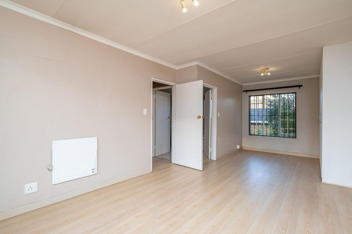 A spacious, empty bedroom featuring light-toned laminate flooring, neutral walls, coved cornicing, and a built-in wall heater with security bars on the window.