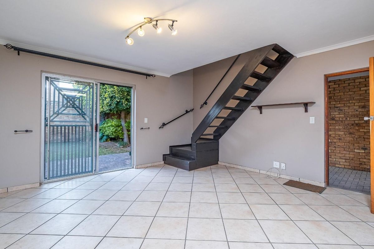 An empty living room featuring tiled flooring, a staircase, and a sliding glass door providing access to the rear garden area.
