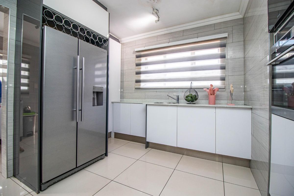Modern kitchen featuring sleek white cabinetry, stone countertops, tiled backsplash, and integrated stainless steel appliances with a dedicated wine storage rack.
