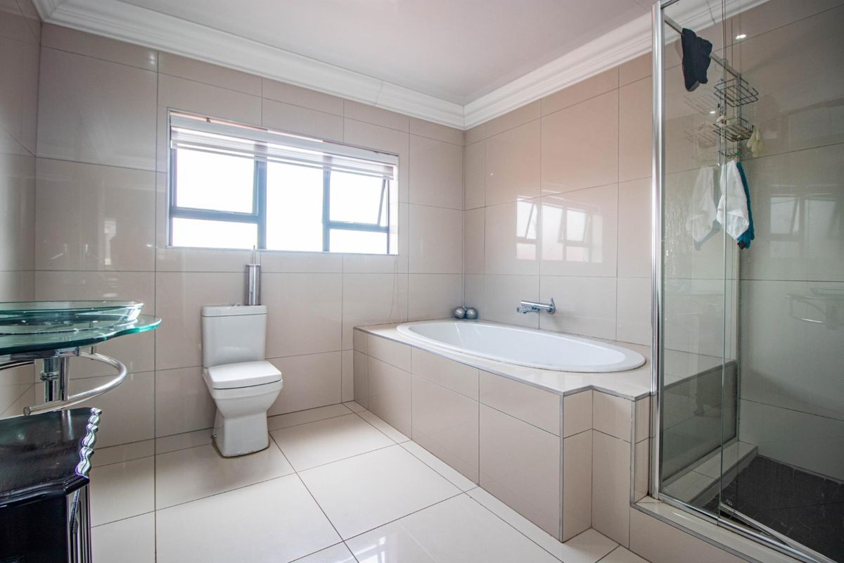 Modern bathroom featuring a built-in bathtub, separate glass shower enclosure, and neutral floor-to-ceiling tiling.
