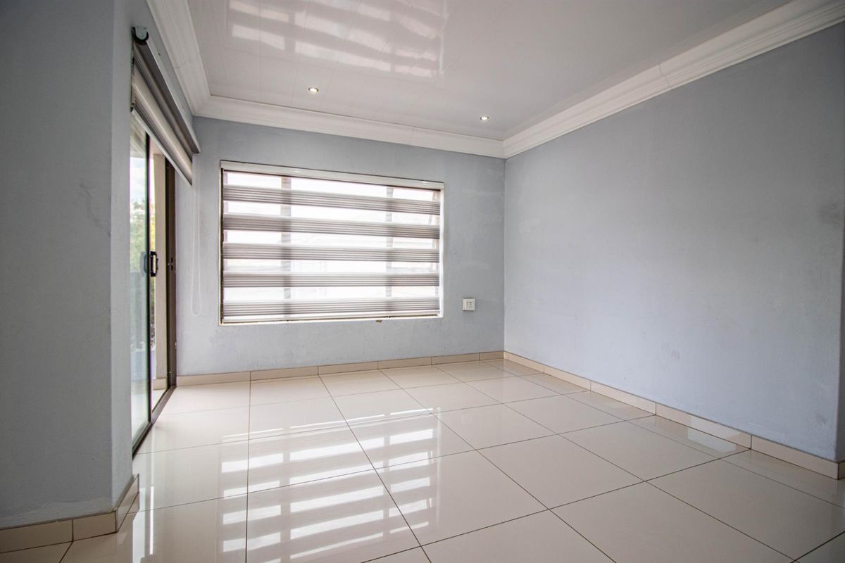 A bright, empty living room featuring neutral tiled flooring, recessed ceiling lights, and a sliding glass door leading to the exterior.
