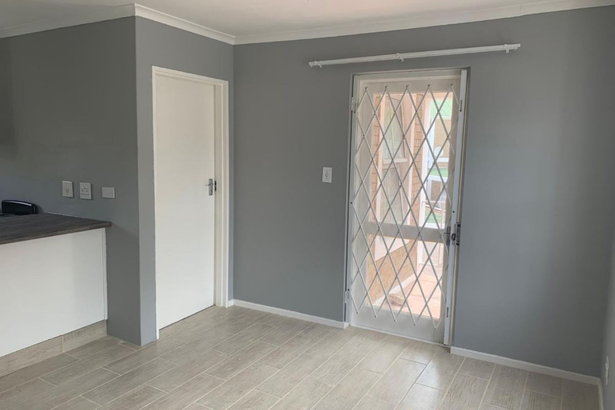 A bright, empty living area featuring neutral grey walls, modern tiled flooring, and a secure metal gate leading to the exterior.