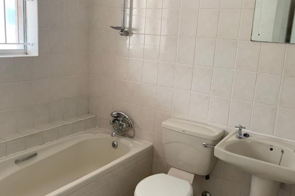 A dated bathroom featuring a bathtub, pedestal basin, and toilet with neutral wall tiling and a window with security bars.