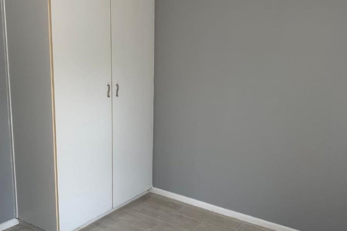 A clean, empty bedroom featuring neutral grey walls, light wood-look tiled flooring, and a built-in wardrobe.