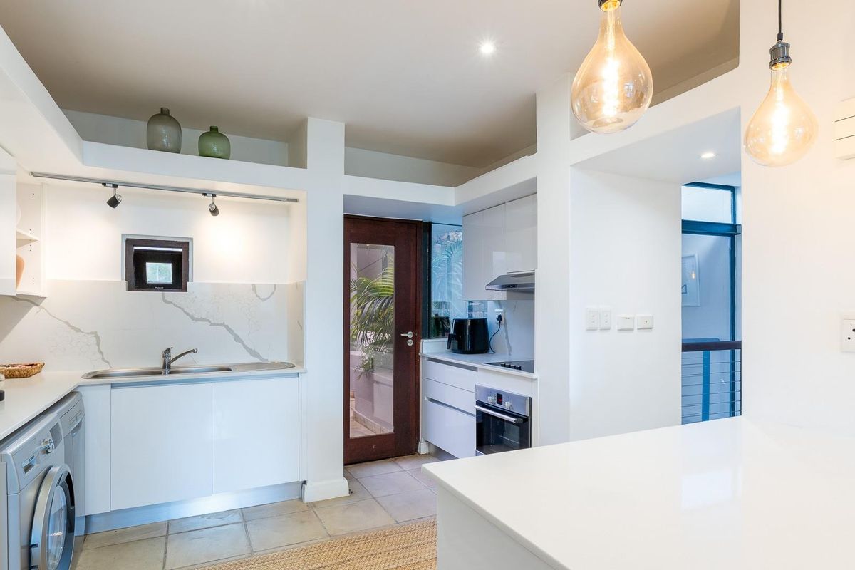 Modern kitchen featuring white cabinetry, stone countertops, integrated appliances, and tiled flooring, with direct access to an outdoor area.