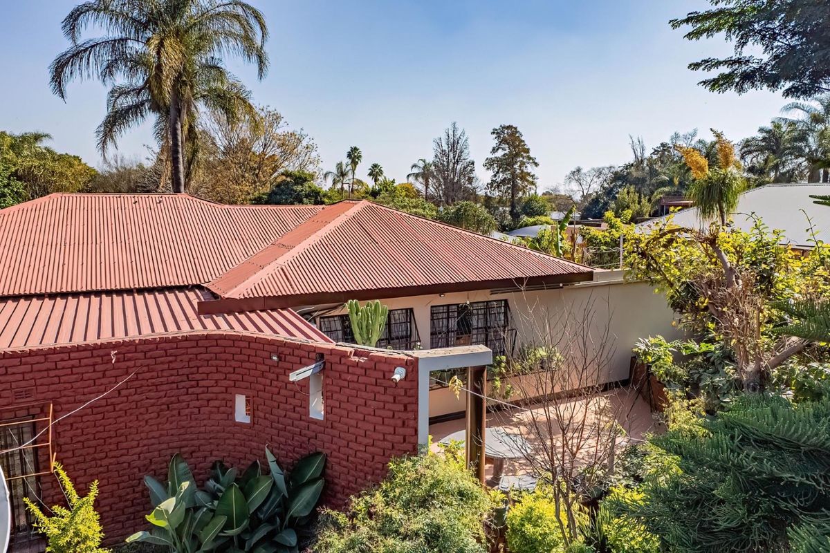 Aerial view of the property showing the corrugated metal roof, exposed brick feature wall, and a paved outdoor patio area surrounded by mature garden.