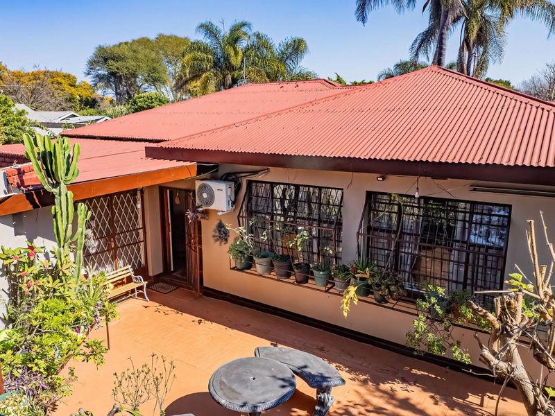 Rear view of the house featuring a tiled patio area, corrugated metal roofing, and security bars on the windows.