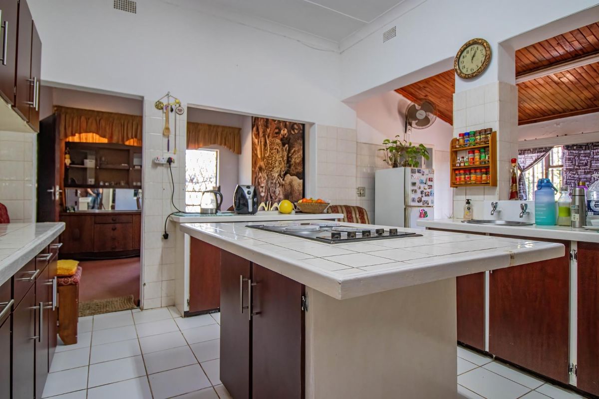 A functional kitchen featuring a central tiled island with a built-in hob, double sink, and ample built-in cabinetry with tiled flooring.