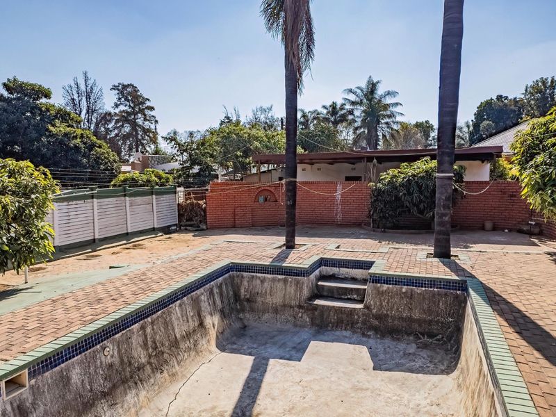 Outdoor pool area featuring a paved surround and brick boundary walls, currently requiring maintenance and refurbishment of the swimming pool structure.