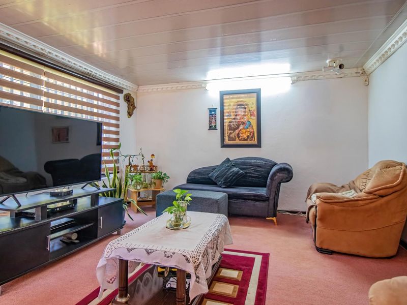 A living room featuring a panelled ceiling with decorative coving and venetian blinds, currently finished with carpet flooring.