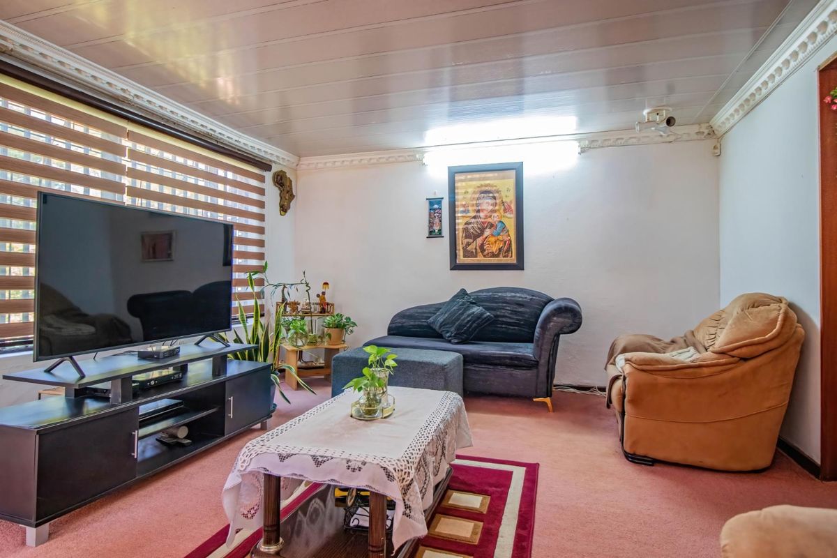 A living room featuring a panelled ceiling with decorative coving and venetian blinds, currently finished with carpet flooring.