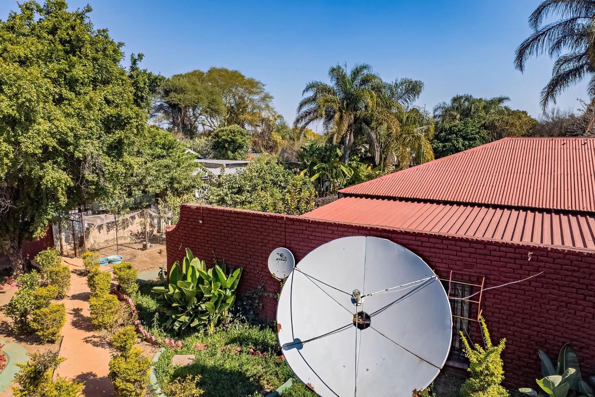 An elevated view of the rear exterior featuring a red brick wall, corrugated metal roofing, and a large satellite dish set within a garden area.