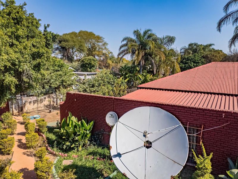 An elevated view of the rear exterior featuring a red brick wall, corrugated metal roofing, and a large satellite dish set within a garden area.