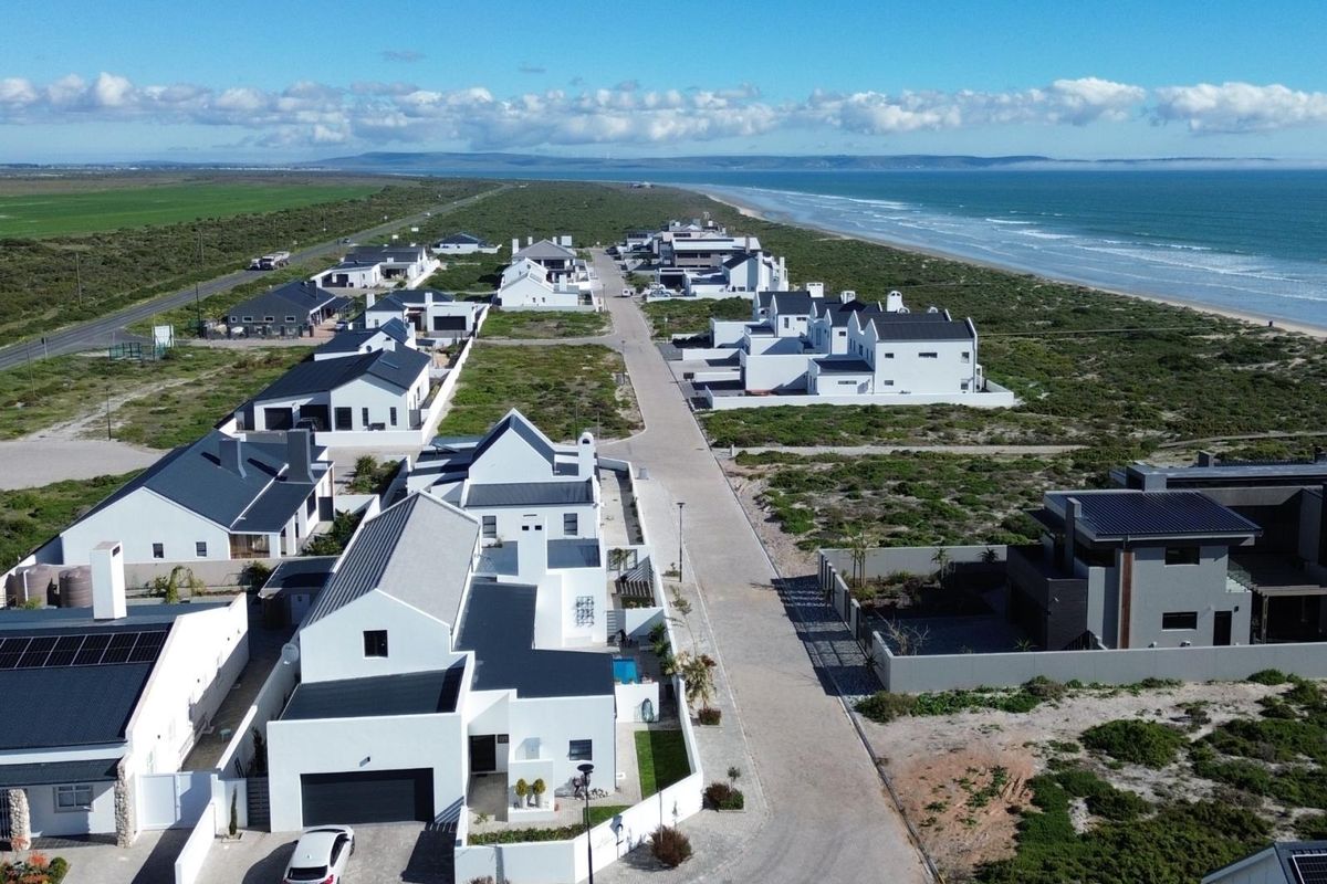 Aerial view of a modern coastal residential estate featuring white homes with dark roofs, situated along the coastline.