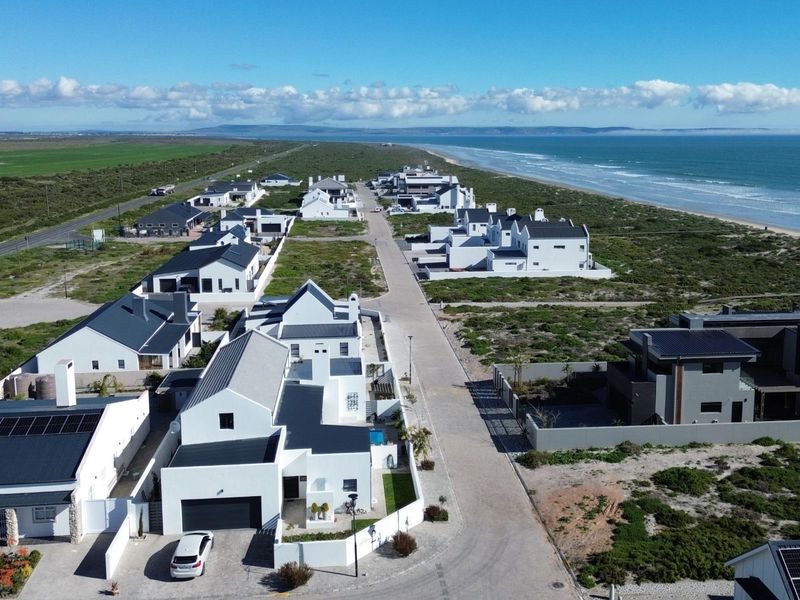 Aerial view of a modern coastal residential estate featuring white homes with dark roofs, situated along the coastline.