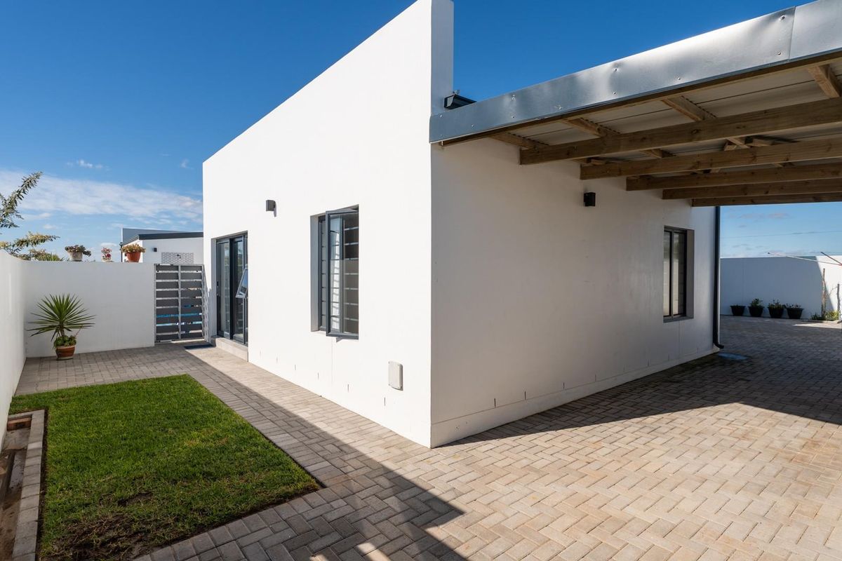 Rear exterior view of the property featuring a paved driveway, covered carport, small lawn, and modern white facade with aluminium window frames.