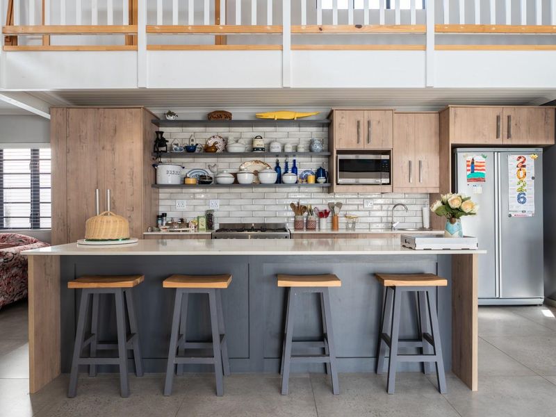 Modern open-plan kitchen featuring a large central island, timber-toned cabinetry, subway tile backsplash, and a mezzanine level overlooking the space.
