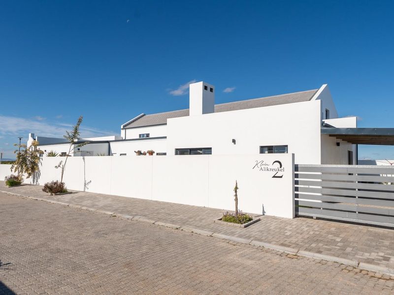 A modern white exterior facade featuring a clean boundary wall, sliding gate, and paved driveway, showcasing a well-maintained contemporary residential property.