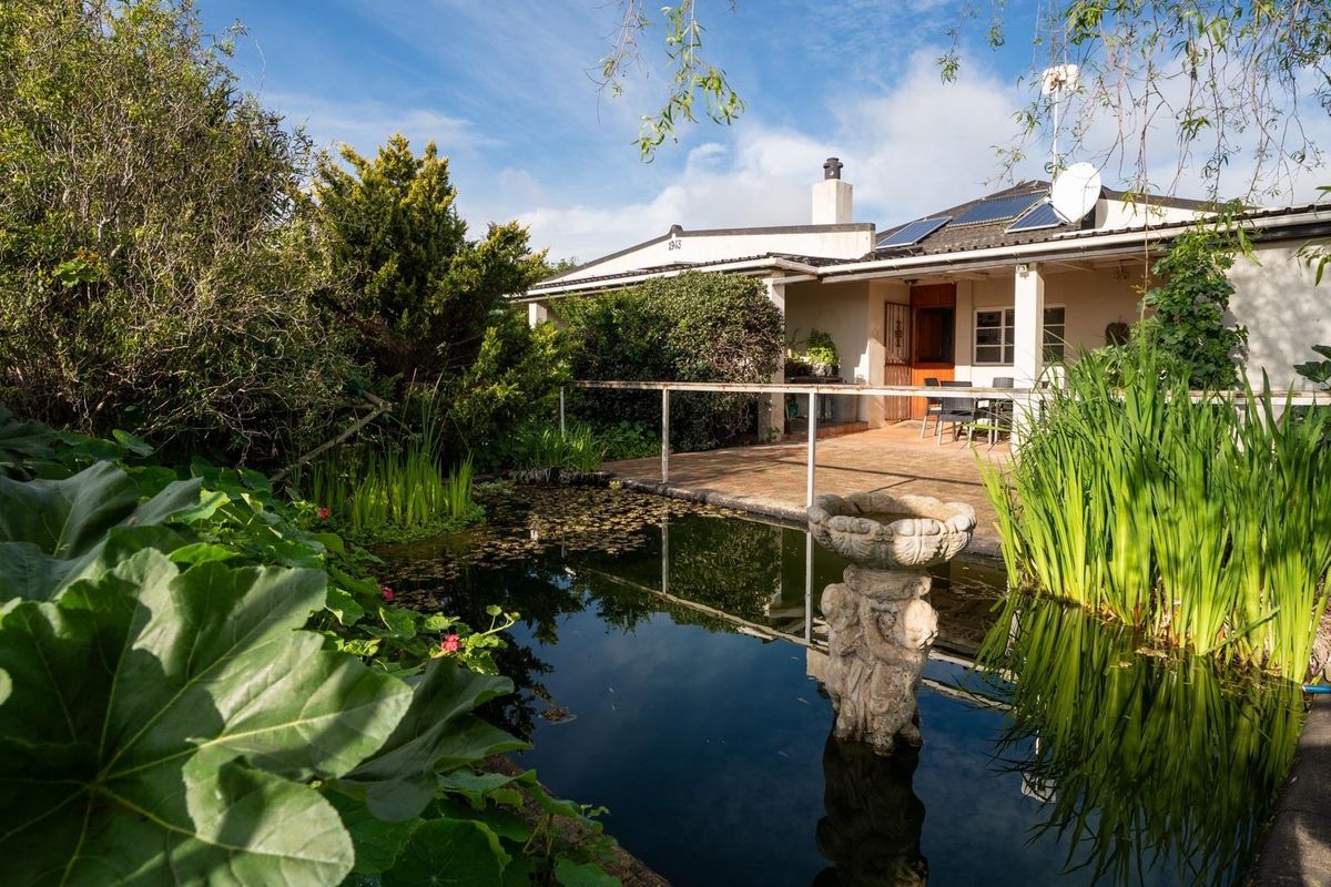 Rear view of the property featuring a landscaped garden with a pond, a tiled patio area, and solar panels installed on the roof.
