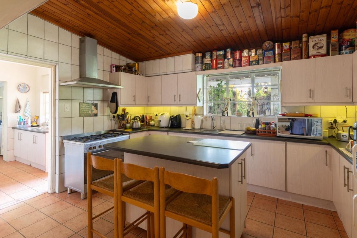 A functional kitchen featuring timber-clad ceilings, laminate cabinetry, a central island, and a gas stove, with an adjacent scullery area visible.
