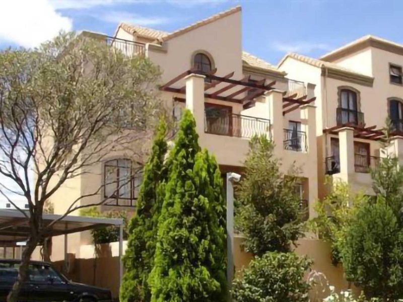 Front elevation of a multi-story residential property featuring arched windows, balconies with wrought iron railings, and a covered carport area.