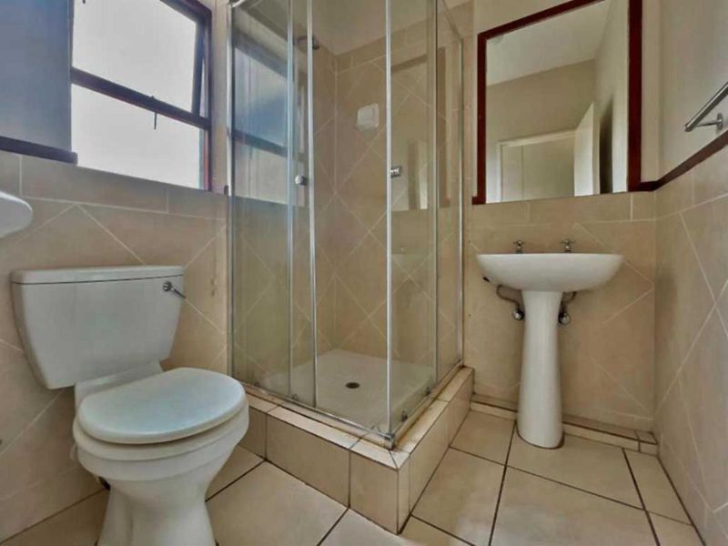 A functional bathroom featuring a pedestal basin, toilet, and a glass-enclosed shower with neutral wall and floor tiling.