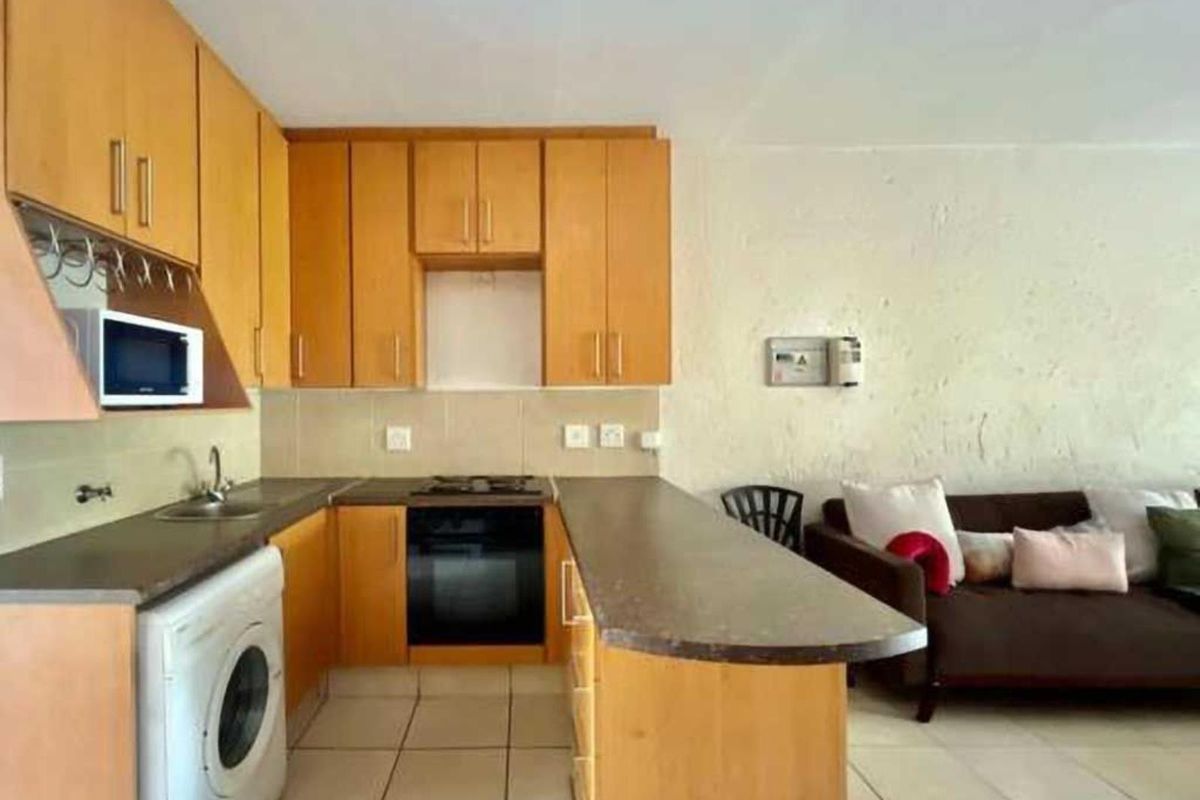 Open plan kitchen featuring light wood cabinetry, built-in oven, gas hob, and tiled flooring, seamlessly integrated with the adjacent living area.