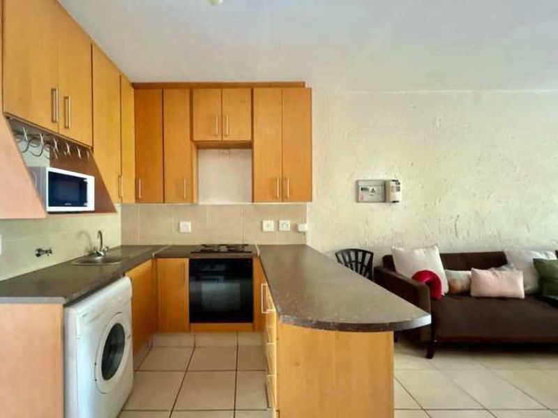 Open plan kitchen featuring light wood cabinetry, built-in oven, gas hob, and tiled flooring, seamlessly integrated with the adjacent living area.