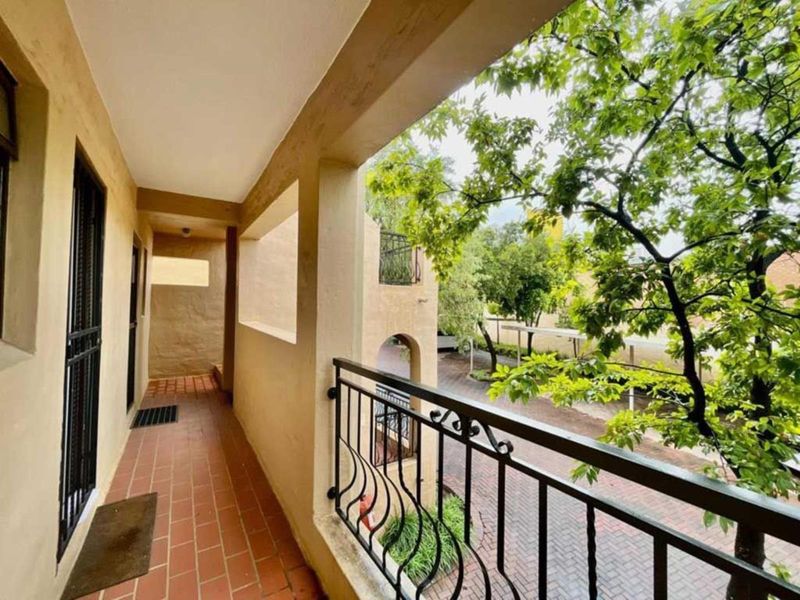 A covered balcony featuring terracotta tiled flooring and a wrought iron railing, overlooking a landscaped garden area.