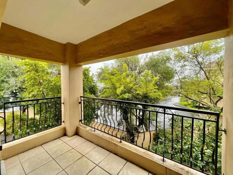 A covered balcony featuring tiled flooring and a decorative wrought iron balustrade, offering pleasant views of the surrounding trees and greenery.