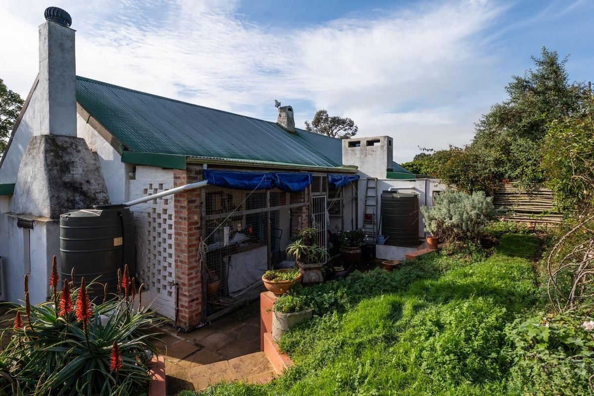 Rear view of the property featuring a corrugated metal roof, brick chimney, and water storage tanks set within a garden area.