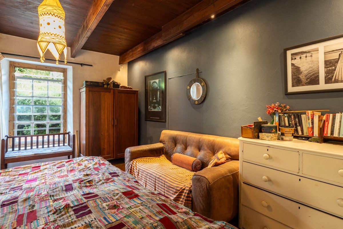 A cozy bedroom featuring exposed timber ceiling beams, warm timber flooring, and a large window providing natural light.