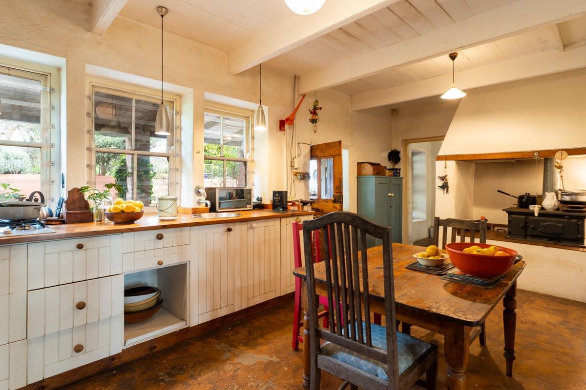 Rustic farmhouse kitchen featuring timber countertops, built-in cabinetry, exposed ceiling beams, and a traditional cast iron stove set within a large fireplace.