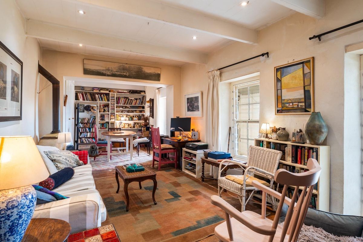 A cozy living room featuring exposed ceiling beams, built-in shelving, and a wood-burning stove, with natural light flowing through sash windows.