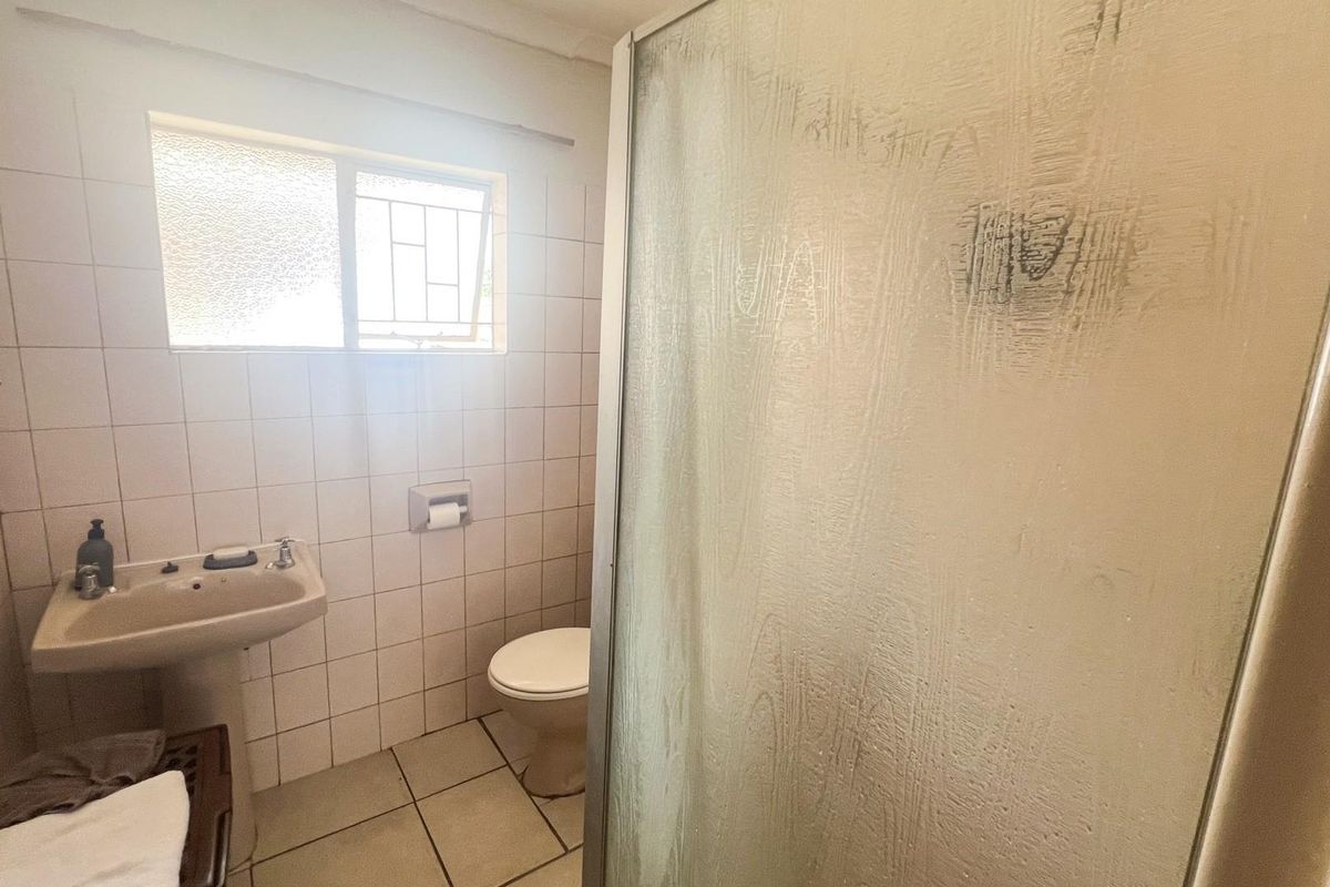 A functional bathroom featuring a pedestal basin, toilet, and a shower enclosure with tiled walls and flooring.