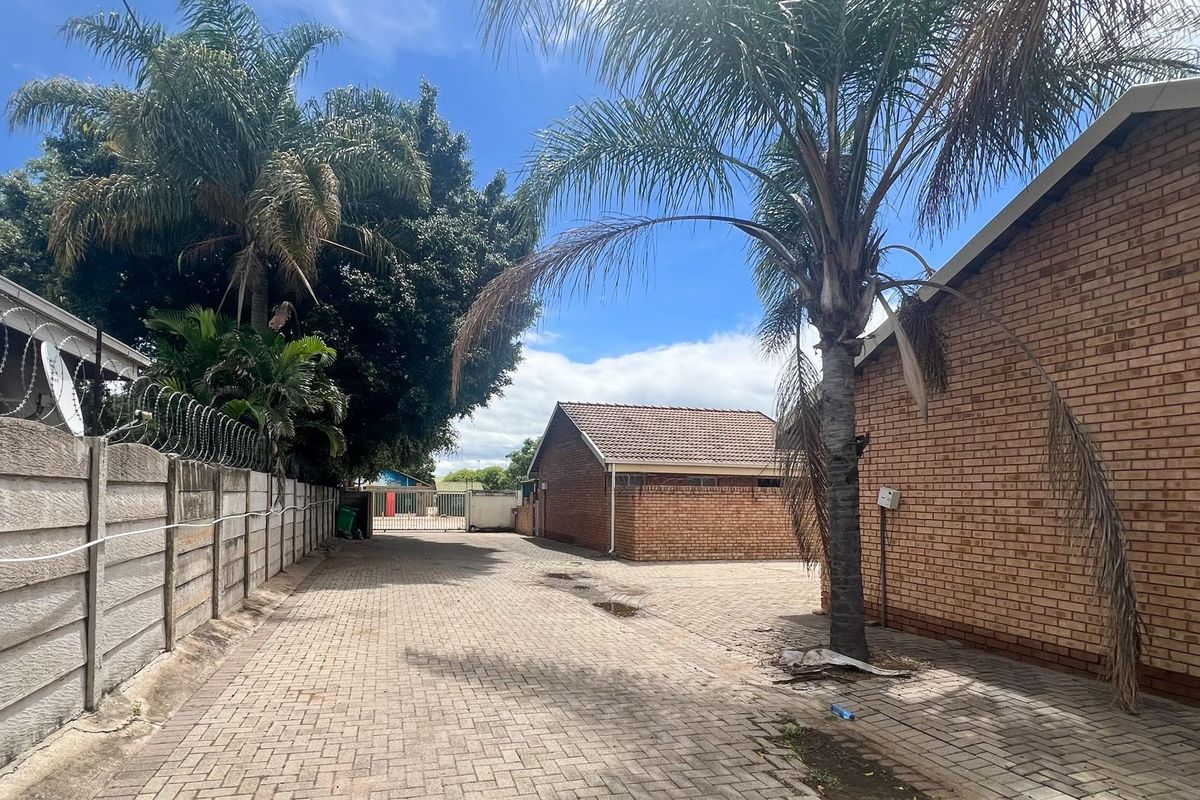 A paved rear courtyard area featuring face brick exterior walls, perimeter boundary fencing with security razor wire, and mature palm trees.