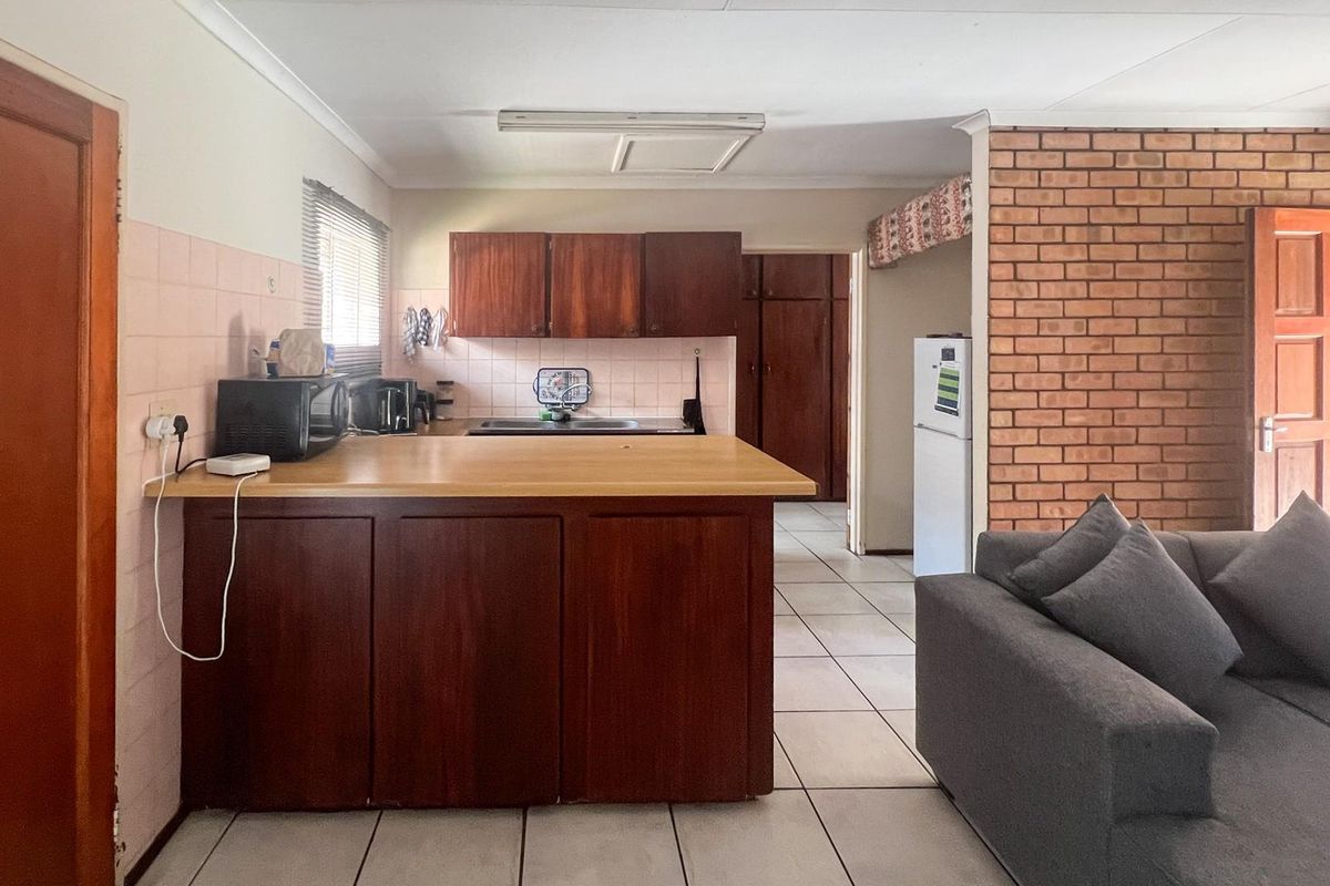 Open-plan kitchen and living area featuring wooden cabinetry, tiled flooring, and an exposed brick feature wall, offering a functional layout with potential for modernization.