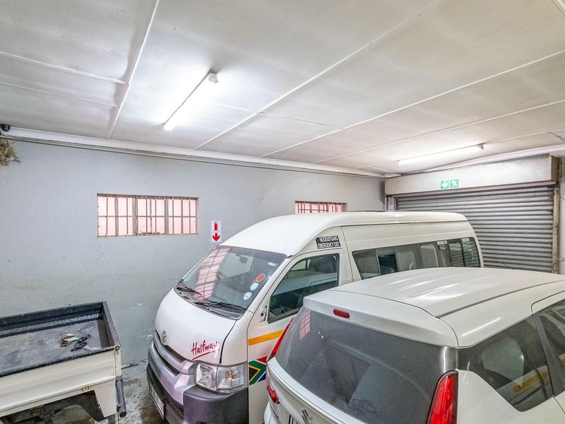 Functional garage space featuring a roller shutter door, fluorescent lighting, and security-barred windows, suitable for vehicle storage or utility use.