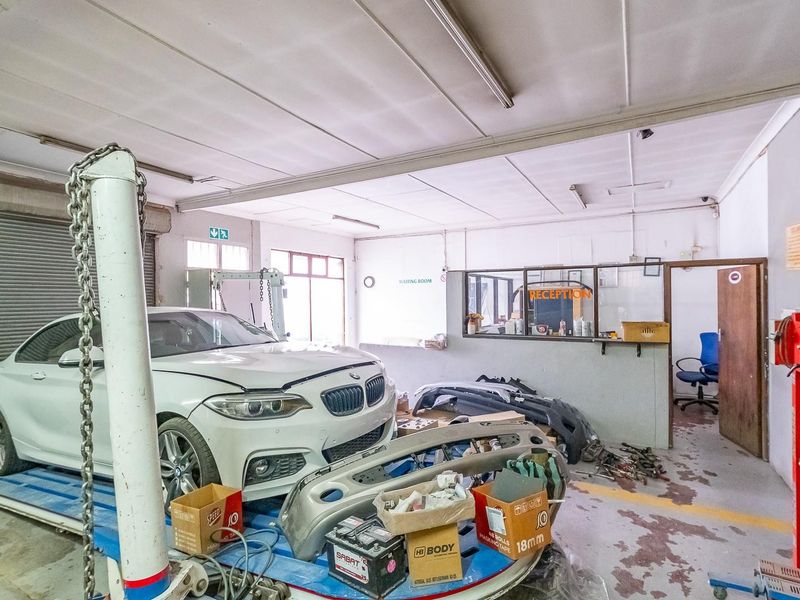 A functional automotive workshop space featuring a roller shutter door, integrated reception area, and industrial concrete flooring.