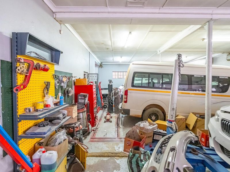 A functional workshop or garage space featuring concrete flooring, overhead fluorescent lighting, and wall-mounted storage systems, suitable for automotive or industrial use.