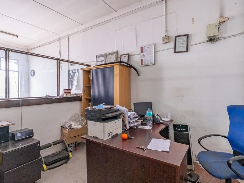 A functional office space featuring a partition wall, exposed electrical conduits, and a drop ceiling, requiring cosmetic updates to improve the overall finish.