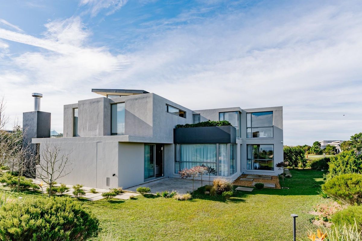 A modern architectural home featuring a concrete facade, large windows, a chimney, and a well-maintained rear garden with a paved patio area.